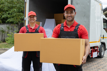 Zwei lächelnde Umzugshelfer in roten Uniformen mit Kartons vor einem Lieferwagen