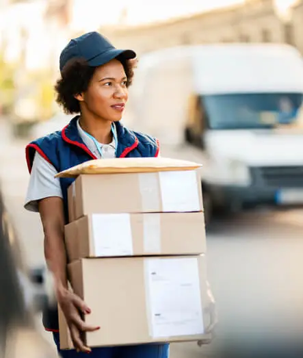 Junge Zustellerin trägt mehrere Pakete vor einem Lieferwagen