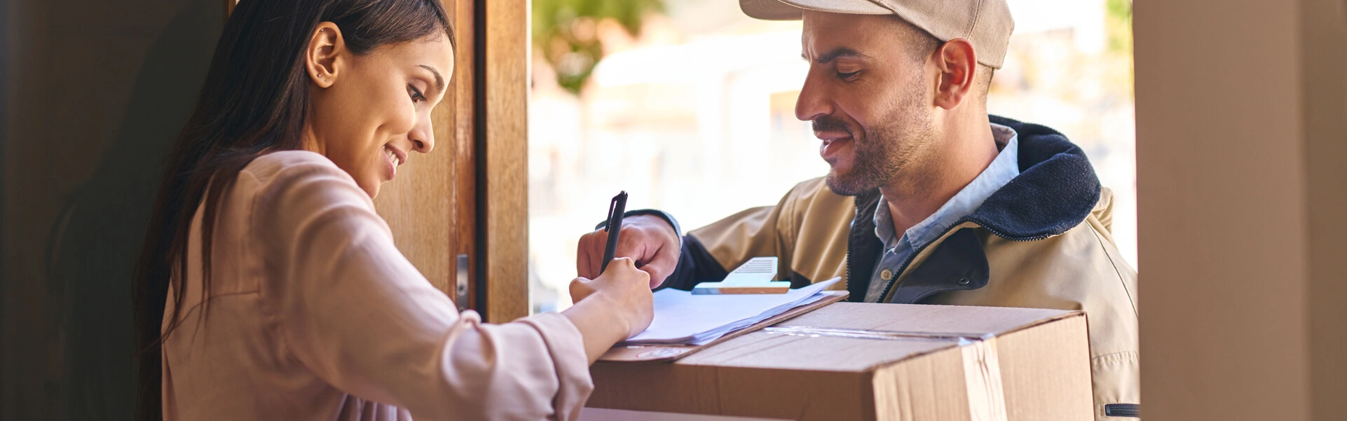 Zusteller übergibt Paket an Kundin, die den Empfang an der Haustür mit einem Lächeln bestätigt